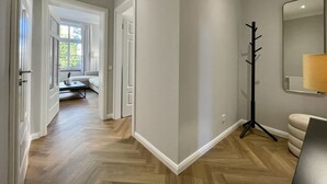 A hallway with a wooden floor, a coat rack, a mirror, and a sofa in the background. - Apartment Villa Anna - Apartment with parking space (Emden)