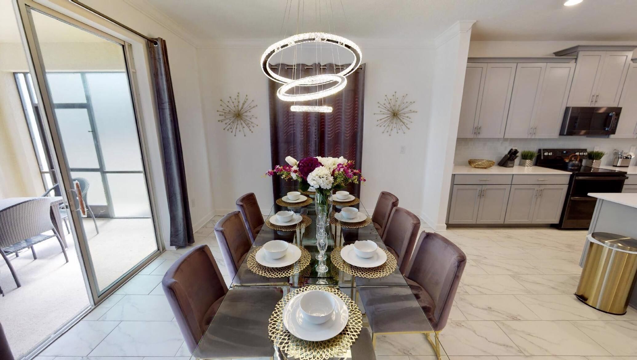 A modern dining area with a glass table, brown chairs, and a decorative light fixture above.