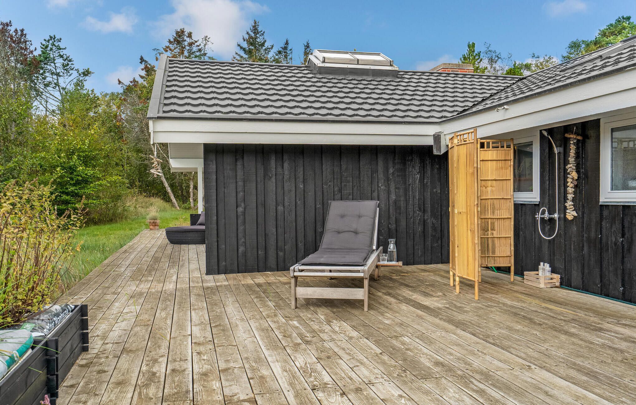 A wooden deck with a lounge chair, a wooden door leading to a shower area, and a tiled roof.