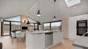 Et moderne køkken med en central ø, store vinduer og et spiseområde med stole.