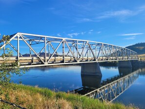 Eine Stahlbrücke über einem ruhigen Fluss unter einem klaren Himmel.
