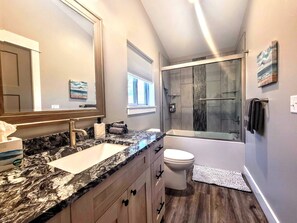 Ein modernes Badezimmer mit einer Granit-Arbeitsplatte, einem großen Spiegel, einer Glasdusche und einer Toilette.