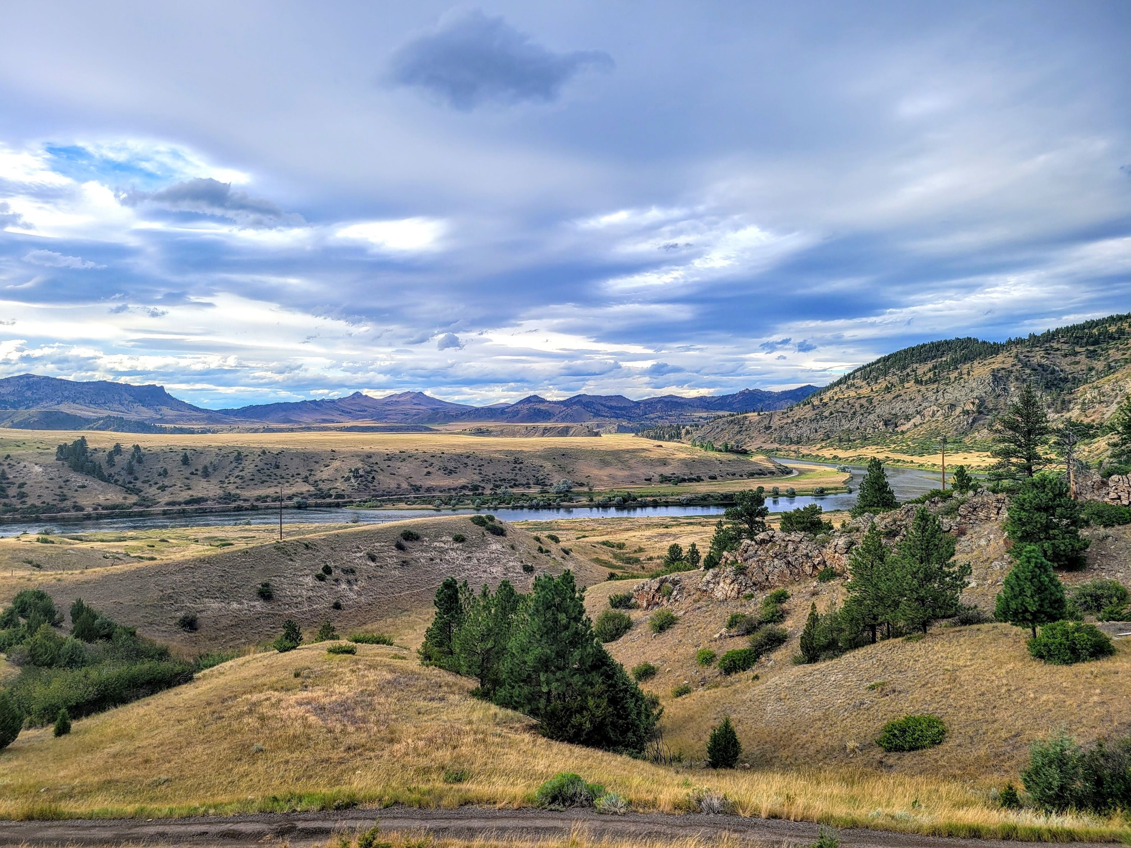 A landscape with a river, hills, and a cloudy sky.