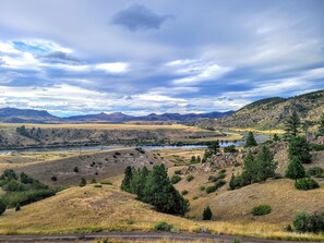 Eine Landschaft mit einem Fluss, Hügeln und einem bewölkten Himmel.