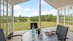 A covered patio with a glass table, two chairs, a bottle, and a small plant. - Gorgeous home in Skjern with WiFi (Skjern)