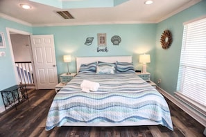 Un dormitorio con cama, dos mesitas de noche, un banco, una puerta y una pared con un cartel que dice 'playa'.