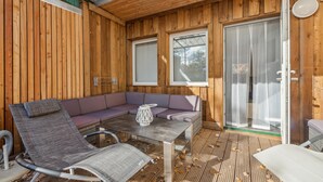 En træhytte med en glasdør, der fører til en balkon, et blødt siddeområde og et bord med en dekorativ vase.