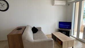 Ein modernes Wohnzimmer mit Sofa, Couchtisch, Holznachttisch, Flachbildfernseher und Wanduhr.