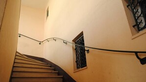 Eine Treppe mit Holzbodenstufen und einem Metallgeländer, die zu einer Zwischenebene mit einem kleinen Fenster mit dekorativen Metallstreben führt.