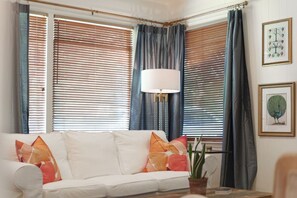 A living room with a white sofa, colorful cushions, a floor lamp, and a potted plant.