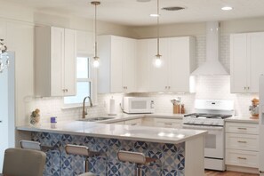 A modern kitchen with white cabinets, a central island, a microwave, stove, and pendant lights.