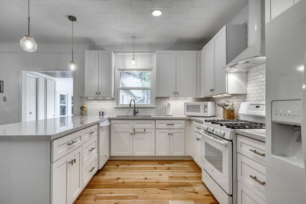 Una cocina moderna con armarios blancos, piso de madera y electrodomésticos de acero inoxidable.