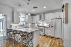 A modern kitchen with white cabinetry, a central island with bar stools, a microwave, stove, and a refrigerator. - Trendy & Posh! Your smalltown retreat awaits! (Bellville)