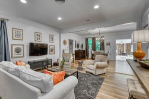 A spacious living room with a sofa, armchairs, a coffee table, and a TV. There is a dining area with a table and chairs in the background. - Trendy & Posh! Your smalltown retreat awaits! (Bellville)