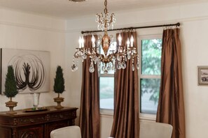 A dining area with a chandelier, brown curtains, a wooden cabinet, and a painting on the wall. - Trendy & Posh! Your smalltown retreat awaits! (Bellville)