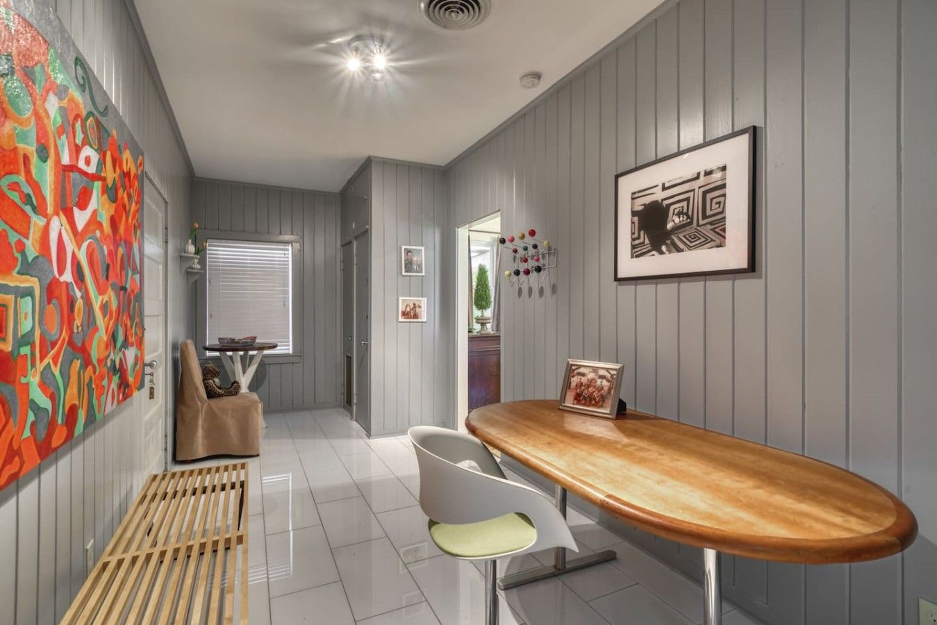 A modern kitchen with a wooden bar counter, a white chair, and a colorful abstract painting on the wall.