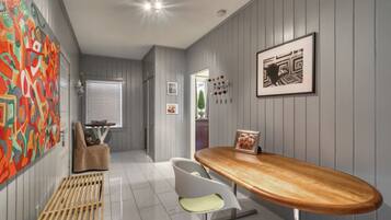 A modern kitchen with a wooden bar counter, a white chair, and a colorful abstract painting on the wall.