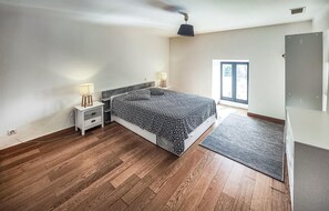 Ein Schlafzimmer mit Bett, Nachttischen, Lampe, Deckenventilator, Fenster und Tür.