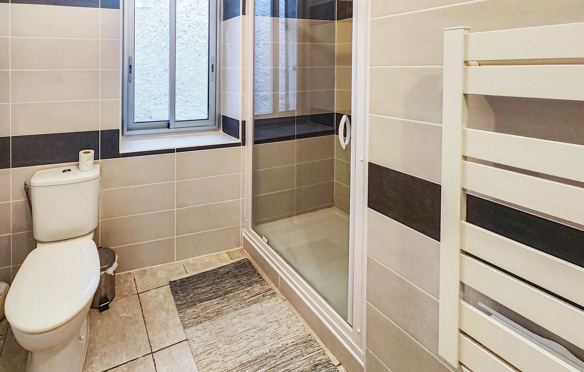 A bathroom with a toilet, a glass shower enclosure, and a window.