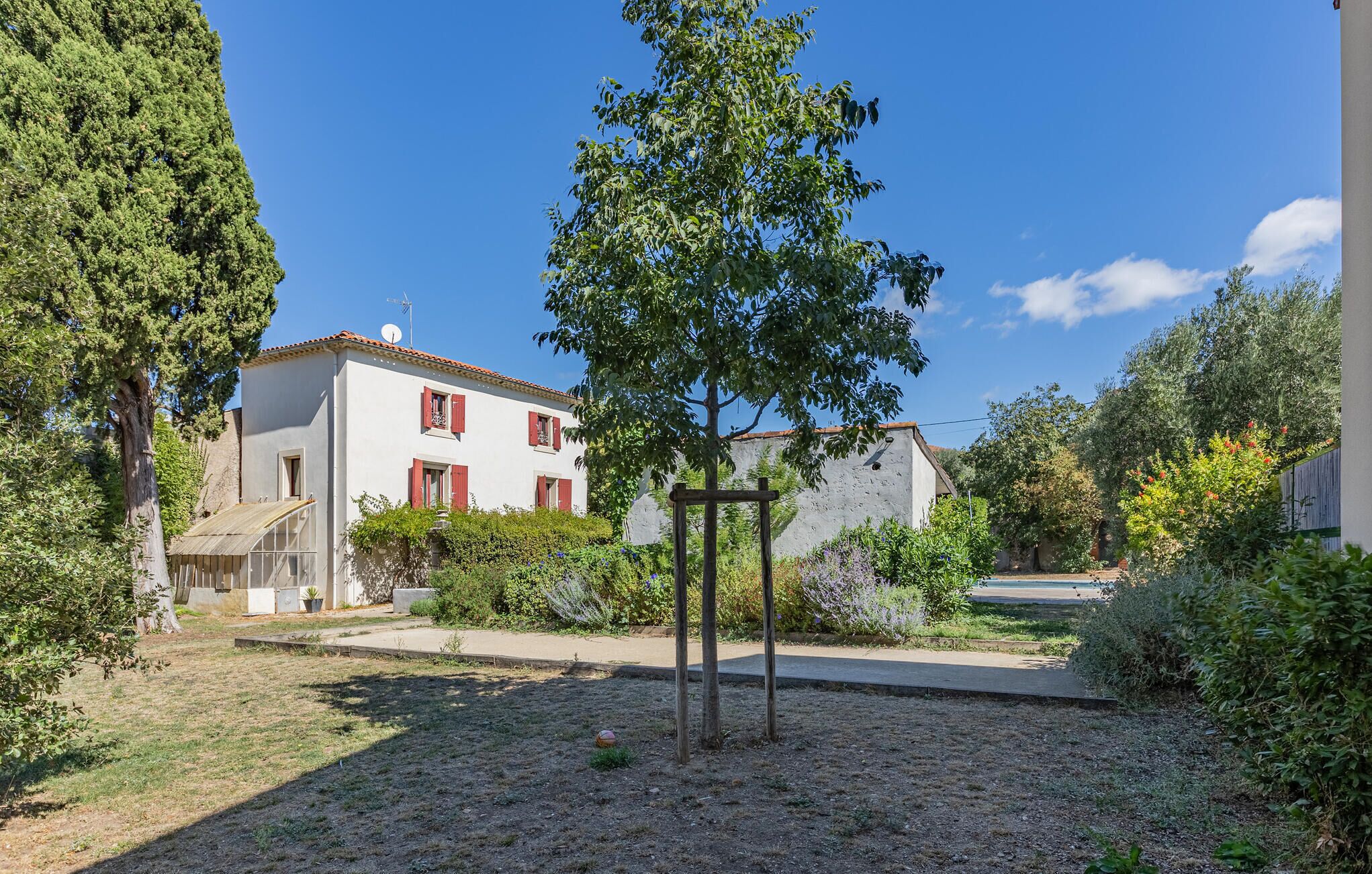 A white building with red shutters, surrounded by greenery and a clear sky.