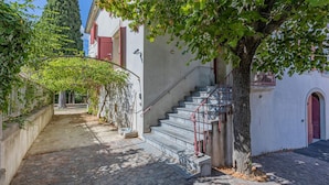 Une ruelle pavée étroite menant à un bâtiment doté d’un escalier et d’un arbre.