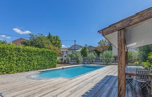 Eine Holzterrasse mit Schwimmbecken, umgeben von Grünflächen und Wohngebäuden.