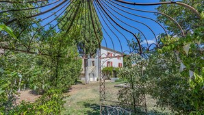 Une maison de campagne rustique, avec un sentier de jardin qui y mène, entourée d’une végétation luxuriante.