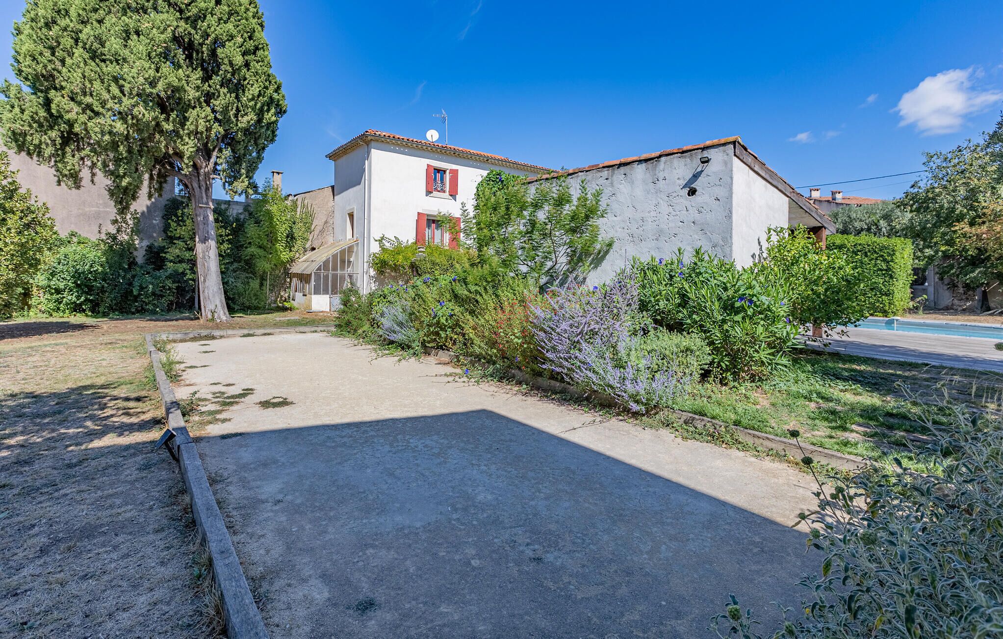 A residential property with a paved driveway, a swimming pool, and a garden with various plants and trees.