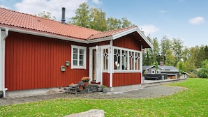 A red wooden house with a tiled roof, a porch with potted plants, and a stone pathway leading to the entrance. - Stunning home in Karlstad with sauna (Karlstad)