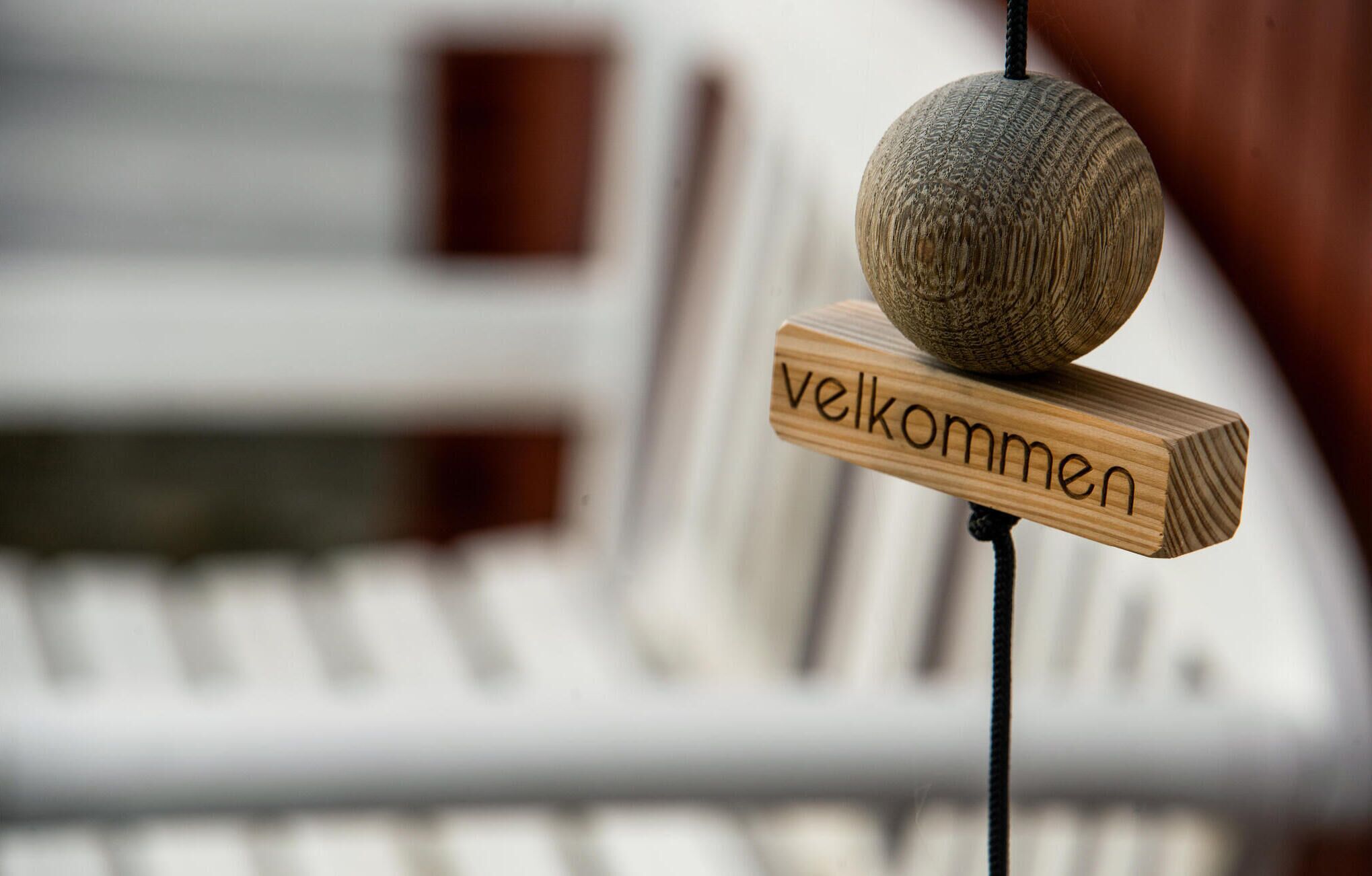 A wooden sign with the word "welcome" in German, a textured spherical object, and a blurred background with a white structure.