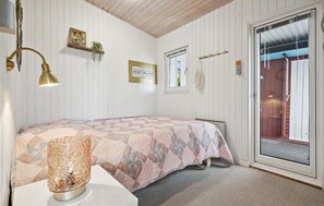 Une chambre à coucher avec un lit, une lampe de chevet, une étagère fixée au mur avec une plante, une fenêtre et une porte donnant sur une vue agréable.