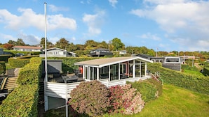 Et moderne hus med et glaskonglomerat, omgivet af velplejede hække og en klar himmel.