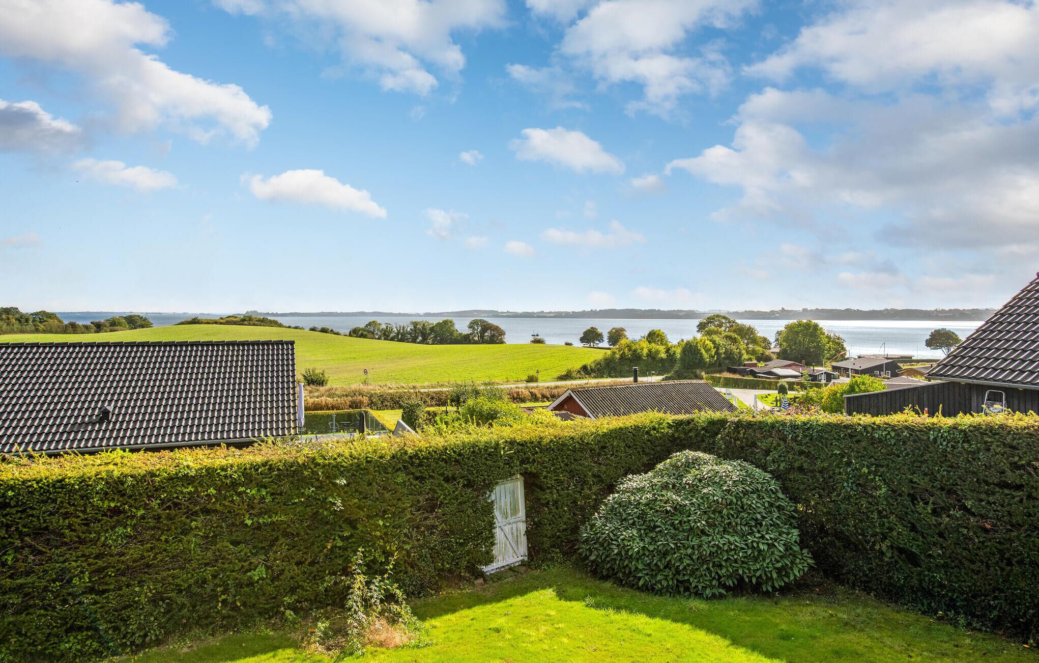 A residential area with a view of a lake, houses with sloped roofs, and a well-maintained hedge.