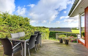 Une terrasse extérieure aménagée avec des meubles en osier, offrant une vue sur un paysage verdoyant et un plan d’eau.