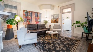 A living room with a sofa, armchair, coffee table, and potted plants.