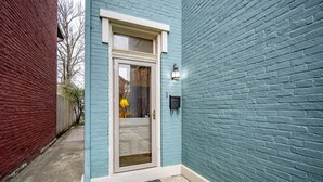 A blue brick building with a white door and a yellow lamp outside.