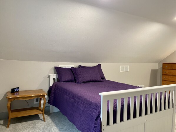 Un dormitorio con una cama, una mesita de noche, un aparador de madera y una cuna blanca.
