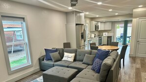Una sala moderna con un sofá modular, una mesa de comedor y una cocina al fondo.
