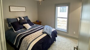 Un dormitorio con cama, ventilador de techo, mesita de noche, ventana y pared con una cita enmarcada.