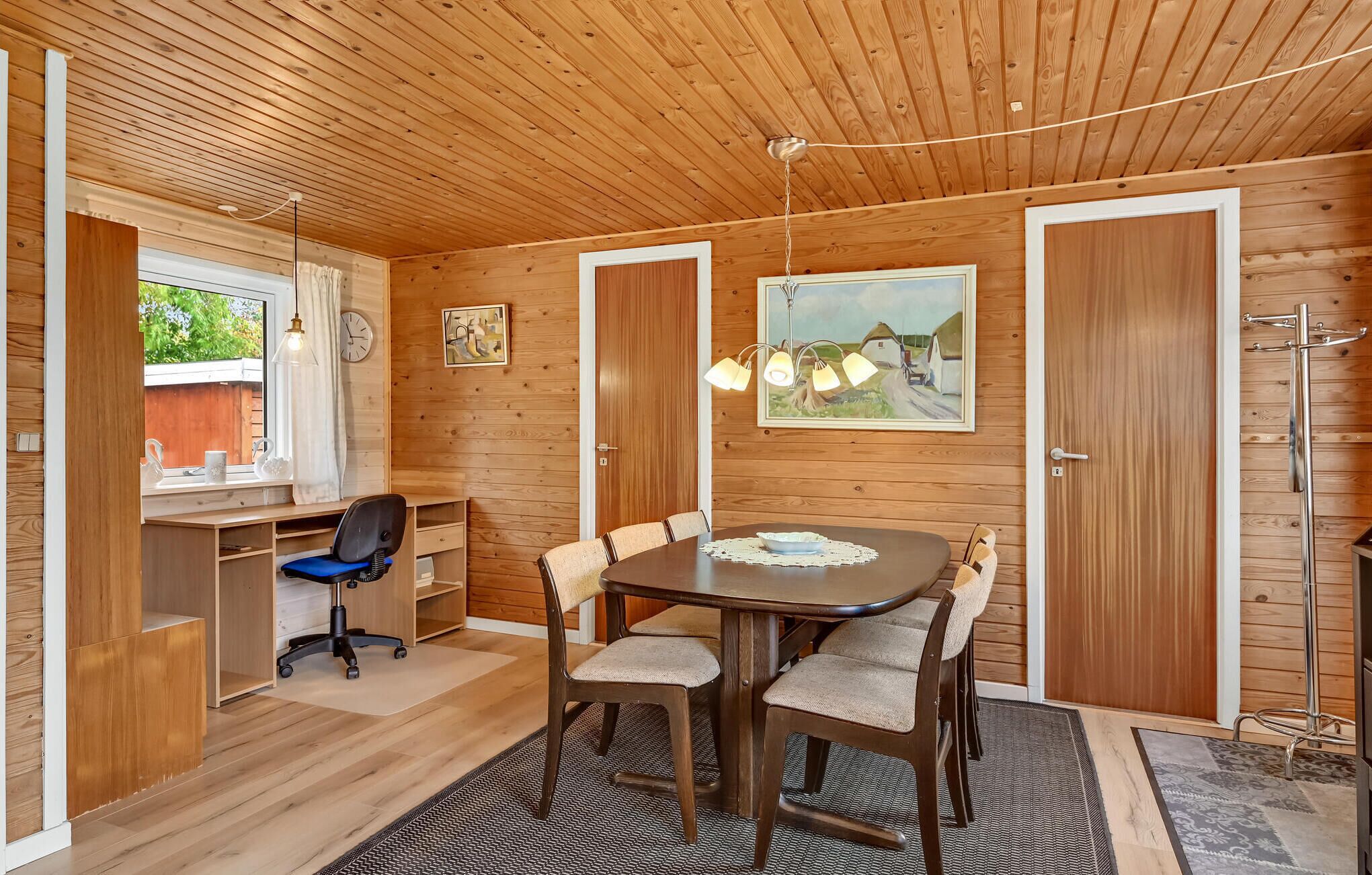 Una habitación compacta con techo de madera, una mesa de comedor con cuatro sillas, un escritorio con una silla y un ventanal grande.