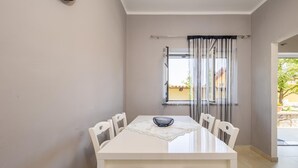 Un coin repas avec une table et des chaises blanches, un bol posé sur la table et une fenêtre avec des rideaux.