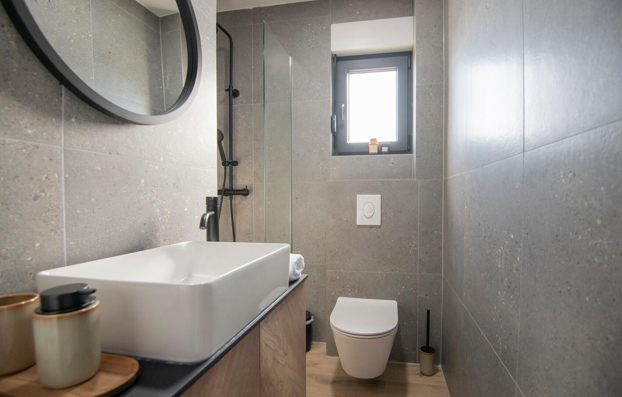 A modern bathroom with a freestanding bathtub, a toilet, and a small window.