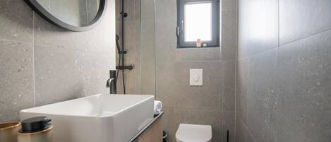 A modern bathroom with a freestanding bathtub, a toilet, and a small window.