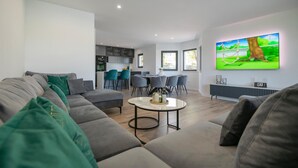 Un salon moderne avec un canapé gris, une table basse et un téléviseur fixé au mur qui diffuse une scène de la nature.