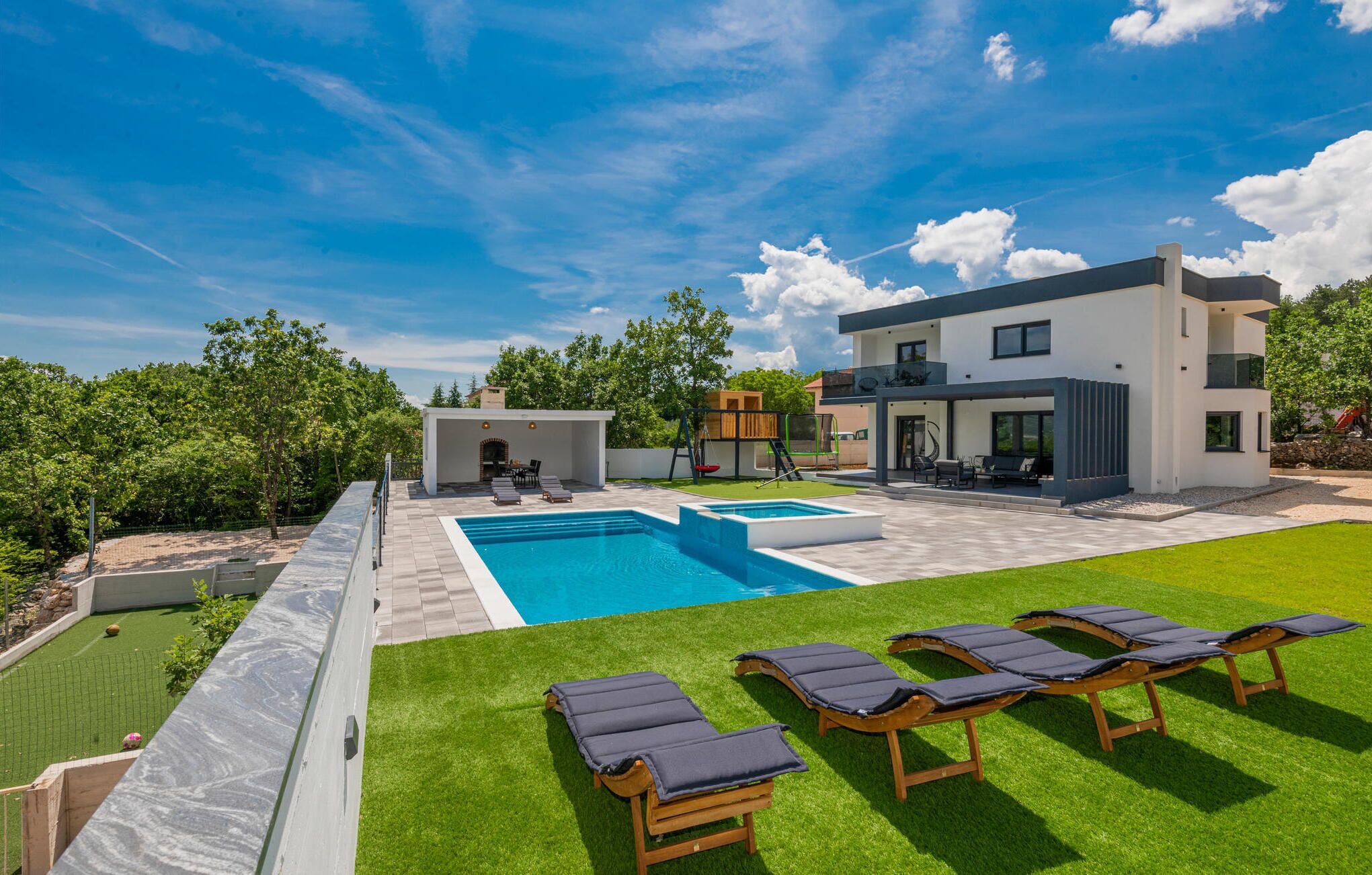 A modern two-story house with a swimming pool, outdoor seating, and a well-maintained lawn.