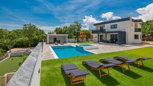 Une maison moderne à deux étages, dotée d’une piscine, d’un espace salon extérieur et d’une pelouse bien entretenue.