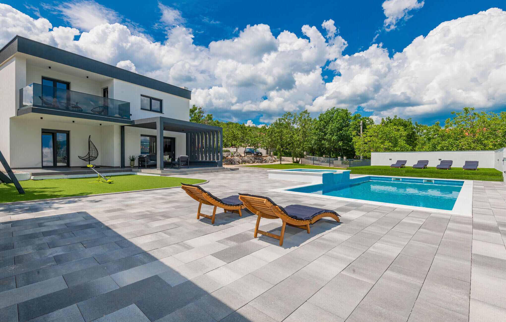 A modern house with a swimming pool, outdoor seating, and a well-maintained lawn.
