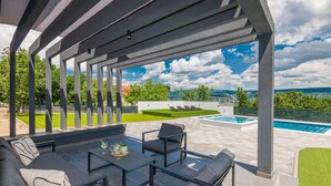Un espace extérieur abrité avec une piscine, des sièges et une vue sur la mer.