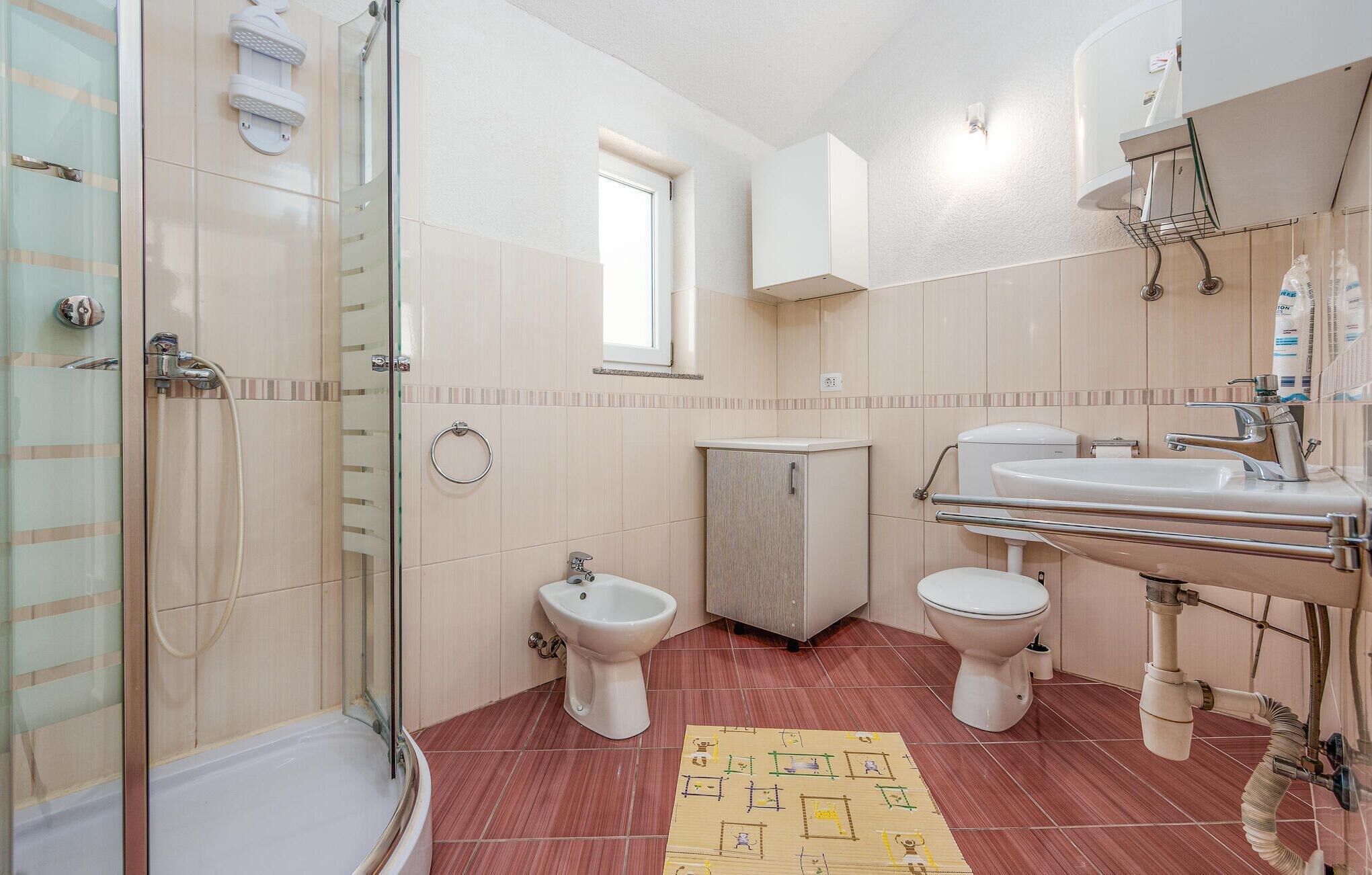 Une salle de bain avec une douche à parois de verre, deux toilettes, un bidet et un lavabo avec un miroir.