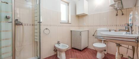 Une salle de bain avec une douche à parois de verre, deux toilettes, un bidet et un lavabo avec un miroir.